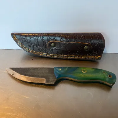Sale Photo Thumbnail #92: Handcrafted fixed-blade knife fashioned from a metal file, featuring a swirl resin handle and a textured brown leather sheath.