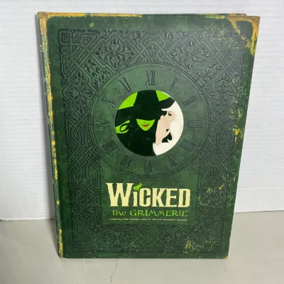 Sale Photo Thumbnail #107: Hardcover companion book, Wicked: The Grimmerie - A Behind-the-Scenes Look at the Hit Broadway Musical. Features an ornate green faux-leather cover with embossed details.