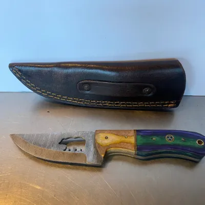 Sale Photo Thumbnail #60: Custom fixed-blade knife featuring a bear silhouette cutout on the steel blade, a multi-colored wood handle, and a dark brown leather sheath.