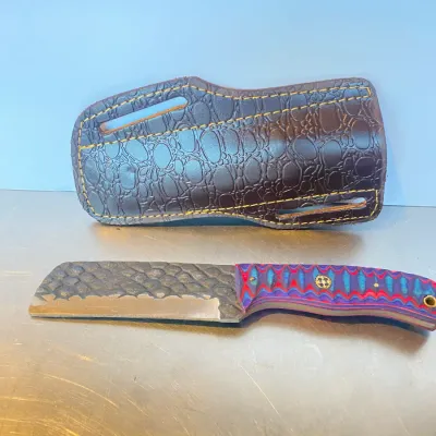 Sale Photo Thumbnail #53: Custom fixed-blade cleaver knife featuring a textured steel blade and a colorful G10 layered handle, paired with a brown embossed leather belt sheath.