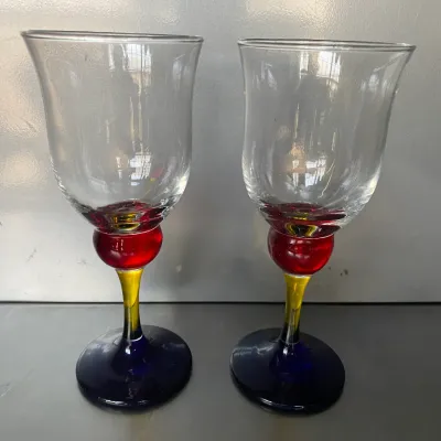 Sale Photo Thumbnail #41: Pair of contemporary hand-blown wine glasses featuring clear tulip-shaped bowls and multi-colored stems in red, yellow, and cobalt blue.