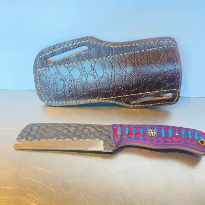 Sale Photo Thumbnail #80: Custom fixed-blade mini cleaver with a textured steel blade, colorful G10 handle scales, and a brown alligator-embossed leather sheath.