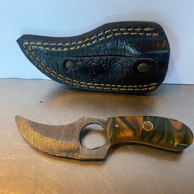 Sale Photo Thumbnail #63: Custom Damascus steel skinning knife with a swirl resin handle and mosaic pin, displayed alongside a black leather sheath.
