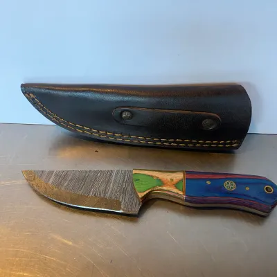 Sale Photo Thumbnail #84: Handcrafted Damascus steel fixed-blade knife featuring a colorful multi-tone wood handle and a dark leather belt sheath.