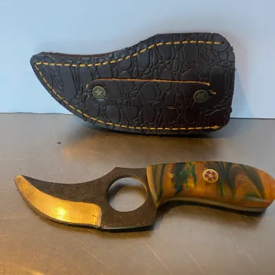 Sale Photo Thumbnail #71: Custom fixed-blade skinner knife with a finger hole, swirl acrylic handle scales, and decorative mosaic pin, shown with a fitted embossed leather sheath.