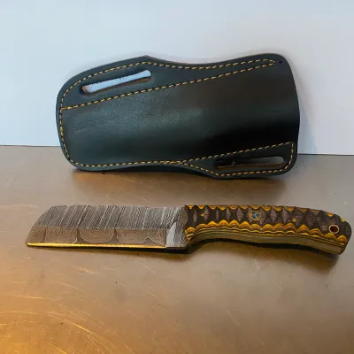 Sale Photo Thumbnail #96: Custom Damascus steel cleaver-style fixed blade knife with a patterned G10 handle and matching black leather sheath.