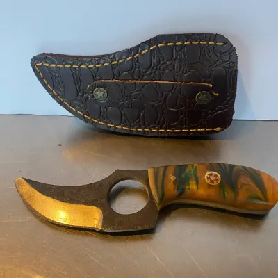 Sale Photo Thumbnail #94: Custom fixed-blade skinner knife featuring a swirled resin handle with mosaic pins, finger hole, and matching dark brown leather sheath.