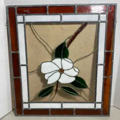 Sale Photo Thumbnail #112: Stained glass panel featuring a central white dogwood flower with green leaves, framed in white and amber glass borders.