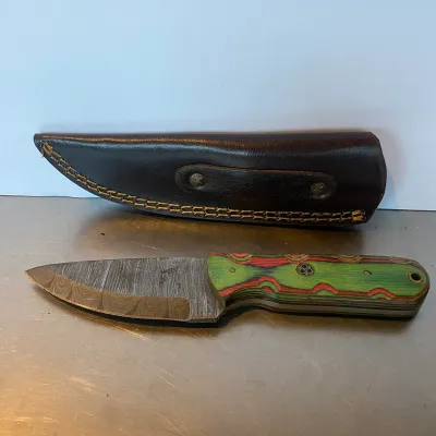 Sale Photo Thumbnail #91: Fixed-blade Damascus steel hunting knife featuring a colorful layered wood or G10 laminate handle and a custom brown leather sheath.
