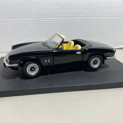 Sale Photo Thumbnail #32: Die-cast scale model of a black Triumph Spitfire convertible featuring a yellow interior and detailed chrome trim, mounted on a display base.