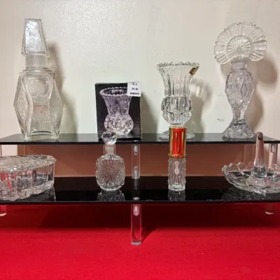 Collection of vintage cut glass vanity items displayed on a black two-tier acrylic riser, including perfume bottles, a ring holder dish,...