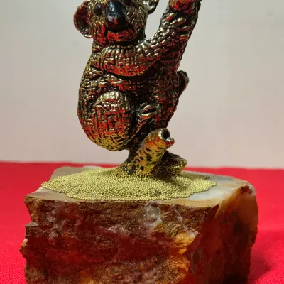Vintage metallic koala figurine perched on a tree branch, mounted on a rough-cut mineral stone base with small golden beads.