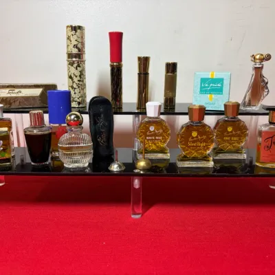 Collection of vintage perfume bottles, atomizers, and boxed fragrances displayed on a two-tiered acrylic riser.