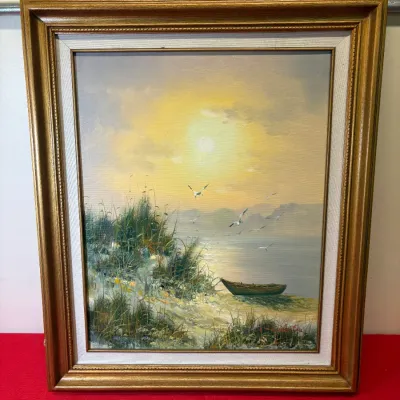 Framed oil painting depicting a coastal sunset scene with a rowboat, sand dunes, and seagulls, signed in the bottom right corner.