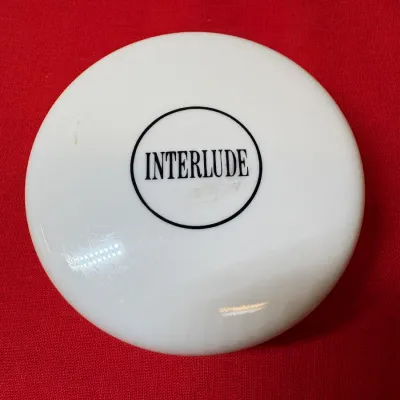 Vintage Frances Denney Interlude white milk glass body powder container lid set against a red fabric background.
