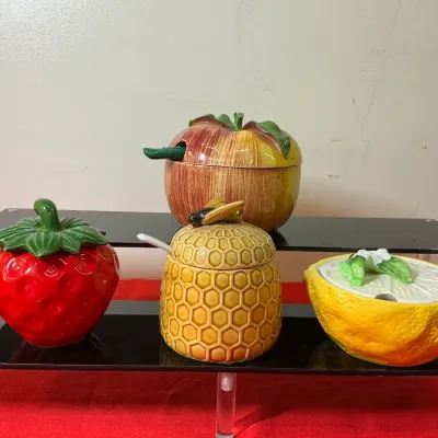 Collection of vintage ceramic jam jars and condiment pots, featuring strawberry, apple, beehive, and lemon designs.