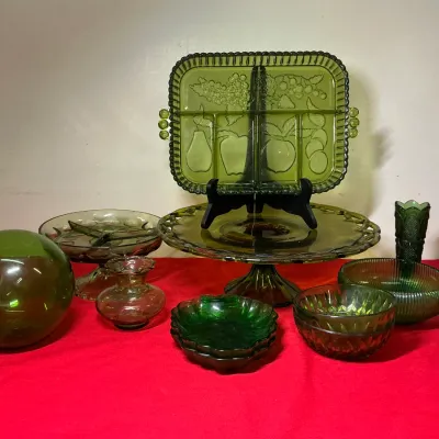 Collection of green glass serving pieces and decor, including a pedaled cake stand, divided tray with fruit motifs, small bowls, and a...