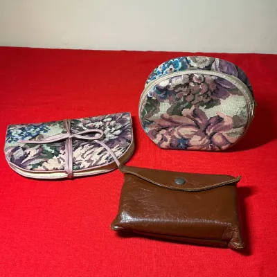 Set of vintage small pouches and cosmetic cases, including two floral tapestry fabric cases and one brown faux-leather snap-closure wallet.