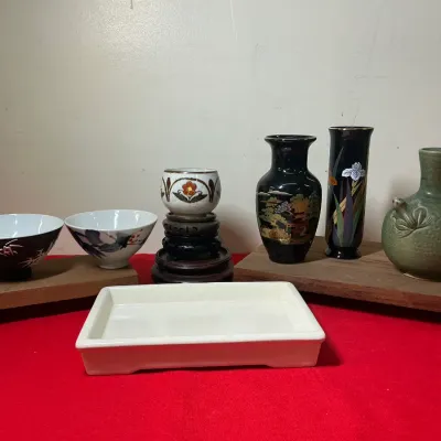 Collection of Asian ceramic items, including small decorative vases, porcelain bowls, wooden display risers, and a white rectangular tray.
