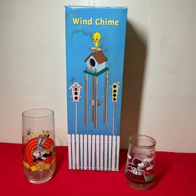 Vintage Tweety Bird wind chime in original box alongside a Bugs Bunny 50th anniversary glass tumbler and a Snoopy drinking glass.