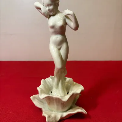 Art Deco style porcelain figurine of a nude female emerging from a flower, finished in an iridescent glaze.