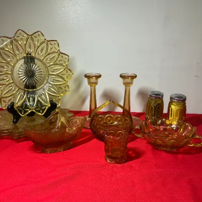 Collection of yellow and amber depression glass pieces, including a starburst display plate, candlestick holders, salt and pepper...