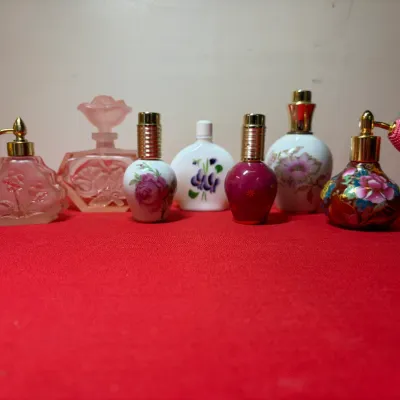 Collection of vintage decorative perfume bottles, including atomizers with fabric bulbs, frosted glass, porcelain, and painted designs.