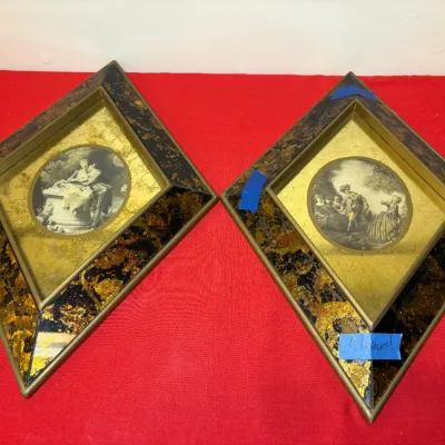 Pair of vintage diamond-shaped framed prints featuring classical courtship scenes with gold leaf accents and tortoise-style marbleized...