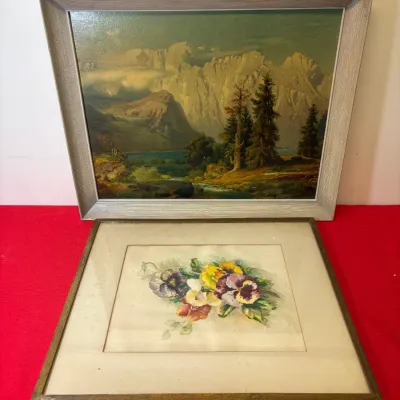 Two framed artwork pieces, featuring a mid-century oil landscape of mountains in a textured silver frame and a vintage floral watercolor...