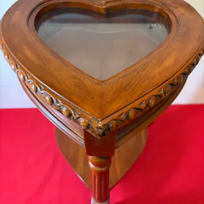 Heart-shaped wooden display side table featuring a glass insert top, carved egg-and-dart rim detail, and a lower shelf.