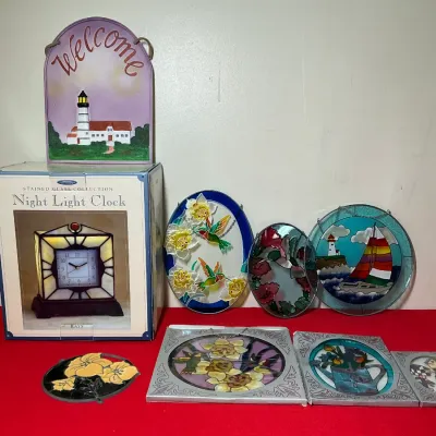 Collection of stained glass suncatchers, framed glass panels, a lighthouse welcome sign, and a boxed stained glass night light clock.