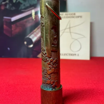 Vintage Steven Augeri patinated brass pocket kaleidoscope with a pocket clip, shown standing vertically on a matching stand with...