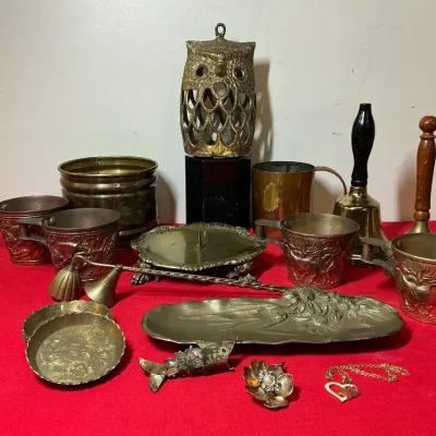 Collection of vintage brass, copper, and metal decorative items, including an owl-shaped lantern, hand bells, embossed cups, a floral...