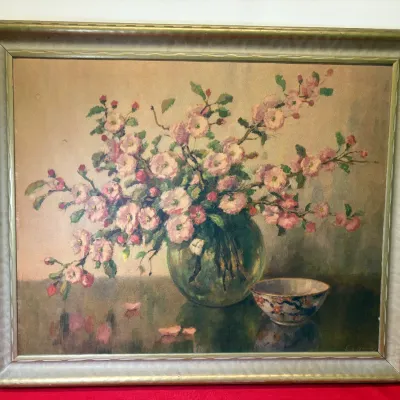 Framed vintage floral still life painting depicting pink blossoms in a round glass vase alongside a small ceramic bowl.