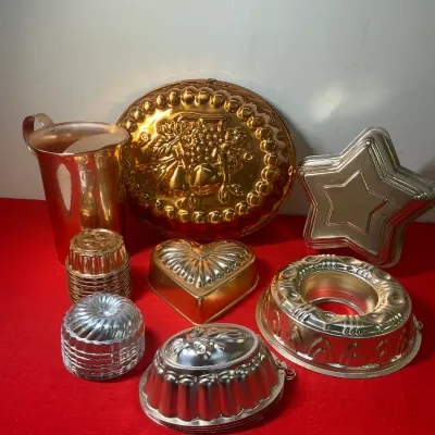 Assortment of vintage metallic baking and gelatin molds in copper and silver tones, including a fruit pattern platter mold, star mold,...