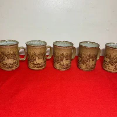 Set of five vintage stoneware coffee mugs featuring a deer scene with a speckled tan glaze and light blue interior accents.