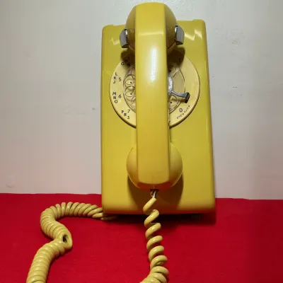 Vintage yellow Western Electric wall-mounted rotary telephone with matching coiled cord.