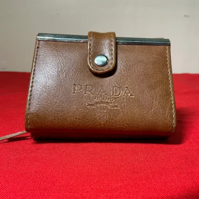 Brown pebbled leather Prada Milano wallet featuring a snap tab closure, silver-tone hardware, and an embossed front logo.