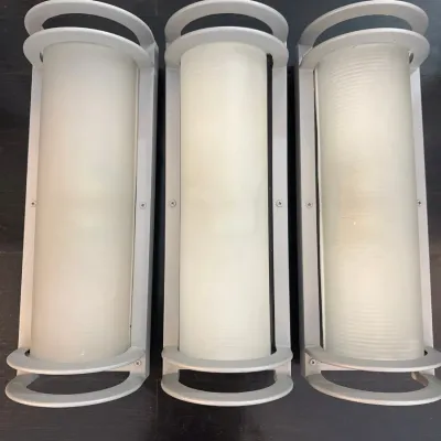 Sale Photo Thumbnail #13: Set of three contemporary outdoor wall sconce light fixtures featuring silver-finished frames and cylindrical frosted glass diffusers.