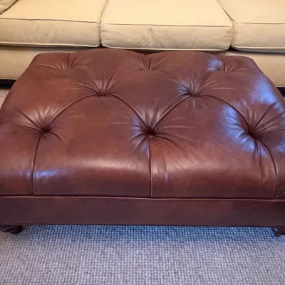 Sale Photo Thumbnail #21: Large button-tufted brown leather ottoman, positioned in front of a neutral upholstered sofa.