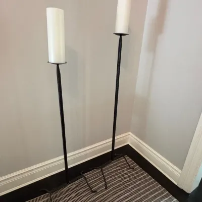 Sale Photo Thumbnail #65: Pair of tall wrought iron floor candle holders with white pillar candles, featuring rustic forged bases.
