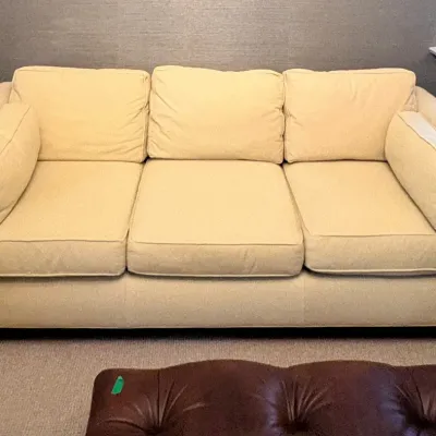 Sale Photo Thumbnail #3: Contemporary cream-colored upholstery three-seat sofa with matching side bolster pillows and dark wood block feet.