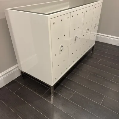 Sale Photo Thumbnail #15: Modern Hollywood Regency style white lacquered sideboard, featuring studded door panels with ring pull hardware, a inset glass top, and sleek chrome square legs.