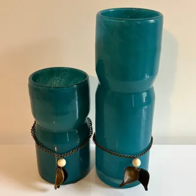 Sale Photo Thumbnail #53: Pair of teal art glass vases featuring an indented waist, each embellished with a brass chain necklace and leaf pendant.