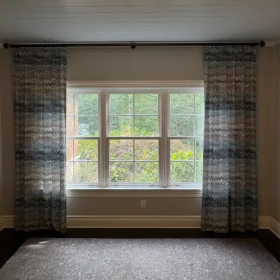 Sale Photo Thumbnail #39: Pair of floor-length drapes with a blue, beige, and grey chevron flame stitch pattern, mounted on a dark metal curtain rod.