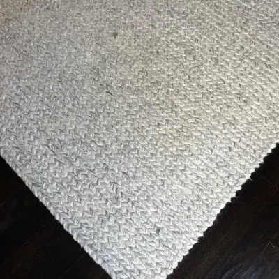 Sale Photo Thumbnail #41: Thick-knit grey and white wool area rug with a braided cable-weave design, laid over dark wood flooring.