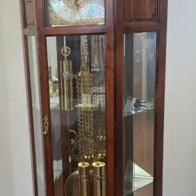 Sale Photo Thumbnail #116: Traditional wooden corner grandfather clock featuring an ornate broken-pediment top with finial, brass pendulum and weights, and side display shelving.