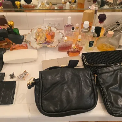 Sale Photo Thumbnail #57: Large collection of vintage perfume bottles, vanity accessories, leather purses, and wallets arranged on a bathroom counter.