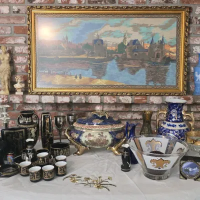 Sale Photo Thumbnail #13: Collection of vintage decorative tableware and collectibles including Greek revival black and gold ceramic items, a large ornate footed tureen, glass bowls, and a framed cityscape needlepoint above a brick mantle.