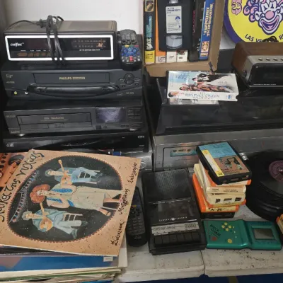 Sale Photo Thumbnail #62: Collection of vintage electronics, home audio equipment, and media, including VCR players, digital alarm clocks, vinyl records, VHS tapes, and 8-track cartridges.